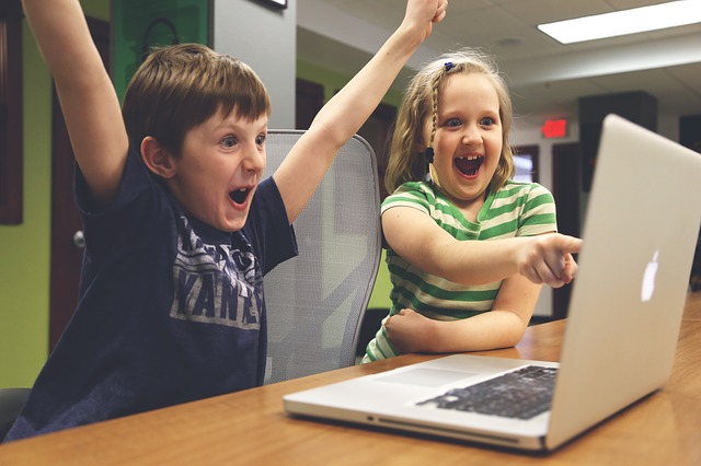 2 children raising arms in victory in front of a laptop